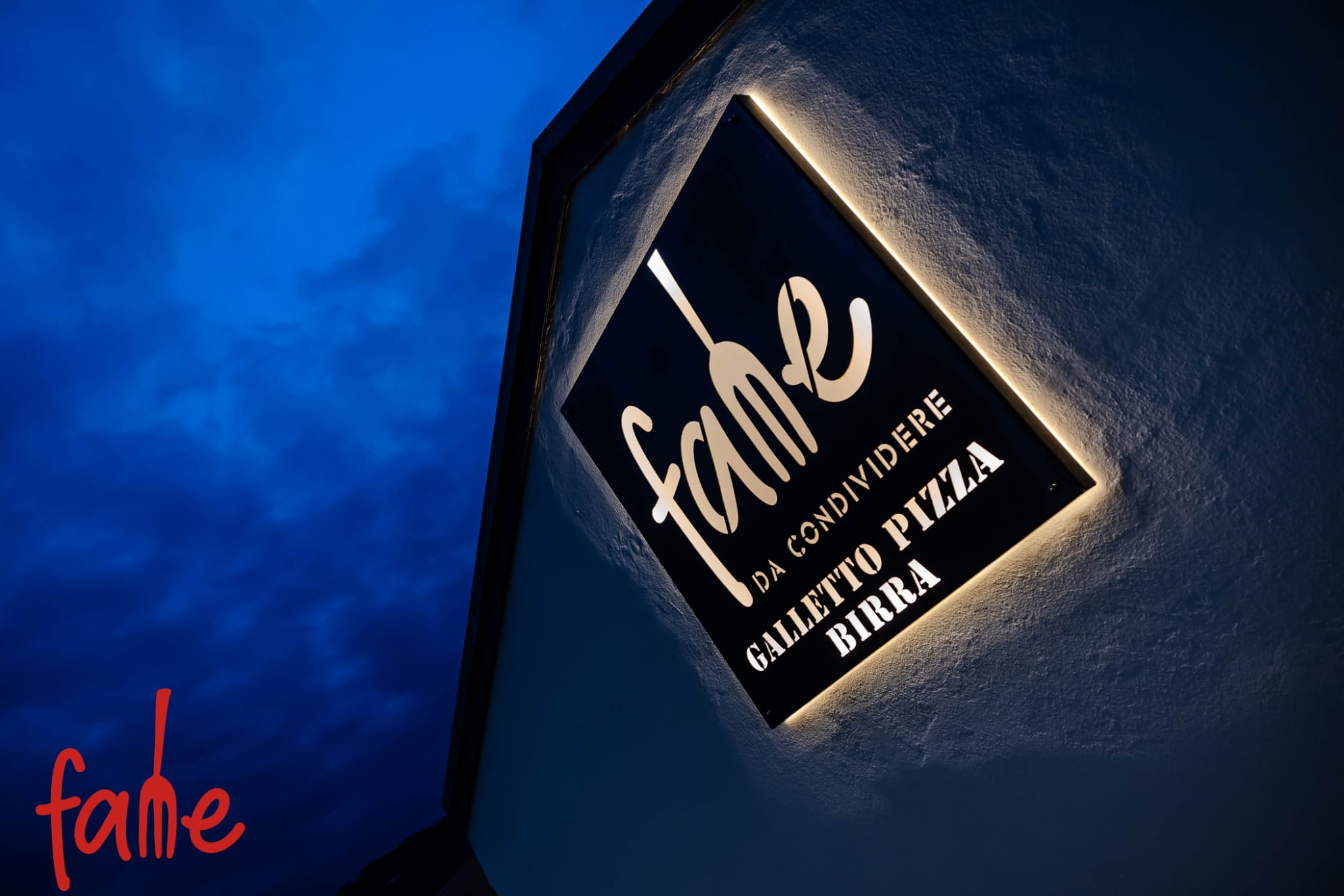 L'insegna illuminata di FAME sul cielo blu della sera